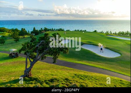 Männliche Touristen im Urlaub schlagen einen Golfball aus einer Sandfalle in der Nähe eines grünen, Port Royal Golfplatz Stockfoto