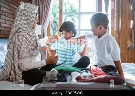 Mutter und ihr Kind bereiten Kleidung und setzen in Koffer für getragen, wenn mudik zurück Dorf nach Hause gehen Stockfoto