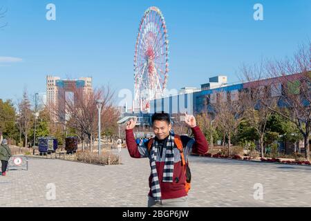 Ein Asain-Mann-Tourist macht ein Foto am Mori-Gebäude mit riesigen Riesenrädern dahinter. Tokio, Japan Februar 8,2020 Stockfoto