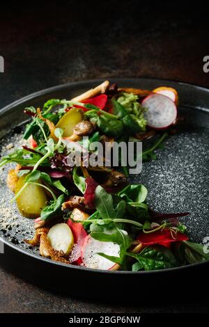 Gesunder Salat aus frischem Gemüse - Tomaten, Avocado, Rucola, Rettich und Samen auf einer Schüssel. Vegane Speisen. Nahaufnahme Stockfoto