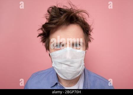 Kaukasischer Mann mit zotteligen Frisur und medizinische Maske skeptisch und unzufrieden Blick auf Quarantäne. Ich brauche dringend einen Friseur Stockfoto