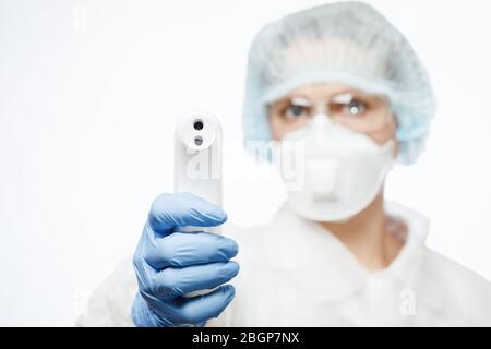 Nahaufnahme eines Arztes, der einen Schutzanzug und eine OP-Maske trägt, mit einem Infrarot-Stirnthermometer oder einer Thermometerpistole, um die Körpertemperatur zu überprüfen Stockfoto