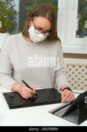 Designerin in Brille und Maske arbeitet von zu Hause aus. Quarantänekonzept. Stockfoto