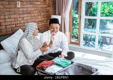 Junges muslimisches Paar, das Kleidung auf dem Koffer für eid mubarak-Urlaub vorbereitet Stockfoto