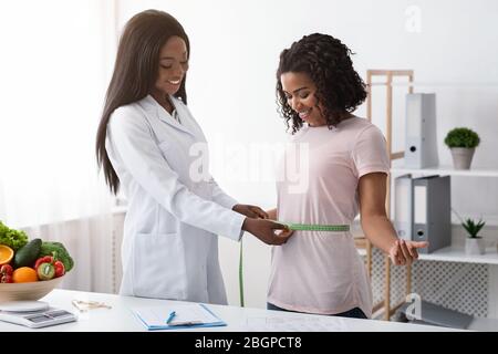 Junge schwarze Frau, die Körpermessungen im Dietologen Büro Stockfoto
