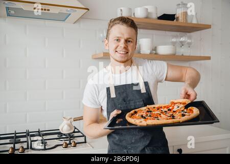 Europäischer Mann hält ein Stück frische Pizza auf hellem Küchenhintergrund Stockfoto