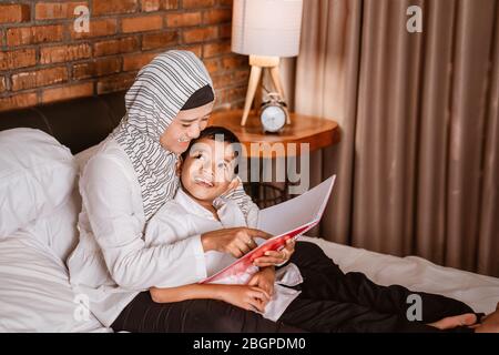 muslimische Mutter liest mit ihrem Sohn während des Schlafens ein Buch Stockfoto