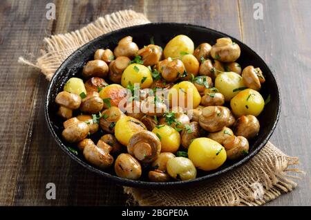 Leckere gebratene Pilze und Kartoffeln in der Pfanne auf Holzhintergrund Stockfoto