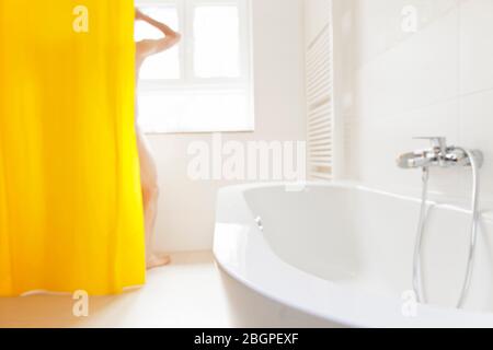 Mann, der in einem hellen Badezimmer mit gelbem Duschvorhang duscht - Fokus auf die Badewanne im Vordergrund Stockfoto