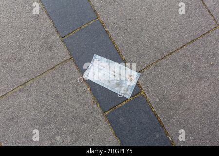 Gebrauchte, weiße OP-Maske auf einem Bürgersteig. Teilweise mit Schmutz bedeckt. Wahrscheinlich verloren oder weggeworfen. Einwegmaske, zur Verhinderung der Virusausbreitung. Stockfoto