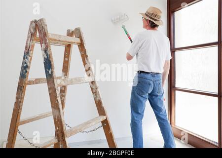 Heimwerker oder professioneller Maler, der ein Zimmer in seinem Haus mit Leiter im Vordergrund malt Stockfoto