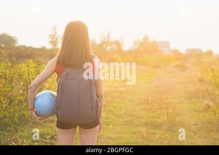 Mädchen mit Rückseitenruck hält Globus im Sonnenuntergang Licht Hintergrund Stockfoto