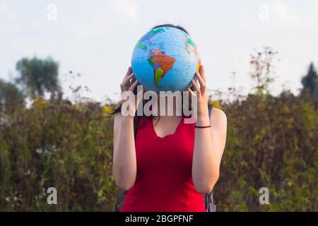 Mädchen mit Rückseitenruck hält Globus im Sonnenuntergang Licht Hintergrund Stockfoto