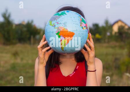 Mädchen mit Rückseitenruck hält Globus im Sonnenuntergang Licht Hintergrund Stockfoto