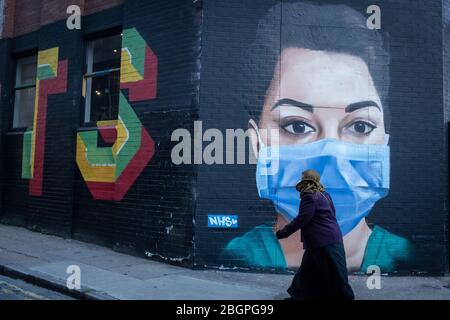 Eine maskierte Frau geht an einem Wandgemälde in Shoreditch East London vorbei, das die NHS-Arbeiter während der Coronavirus-Pandemie feiert. Stockfoto