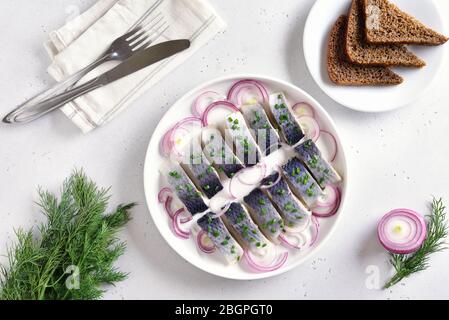 Gesalzener Hering mit Gewürzen, Kräutern und Zwiebeln auf Teller auf weißem Steingrund mit Kopierraum. Russische Küche. Draufsicht, flaches Lay Stockfoto