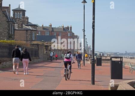 Portobello, Edinburgh, Schottland, Großbritannien. April 2020. Sehr ruhige Promenade und Strand, Temperatur 11 Grad mit Wind ENE 15mph, mögliche Böen von 23 mph, wie die NHS danke Flagge zeigt. Fußgänger mischten sich mit Radfahrern auf der Promenade oft zu eng für richtige körperliche soziale Distanz und wenige Menschen am Sandstrand. Quelle: Arch White/Alamy Live News. Stockfoto