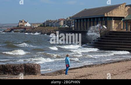 Portobello, Edinburgh, Schottland, Großbritannien. April 2020. Sehr ruhige Promenade und Strand, Temperatur 11 Grad mit Wind ENE 15mph, mögliche Böen von 23 mph, wie die NHS danke Flagge zeigt. Fußgänger mischten sich mit Radfahrern auf der Promenade oft zu eng für richtige körperliche soziale Distanz und wenige Menschen am Sandstrand. Quelle: Arch White/Alamy Live News. Stockfoto