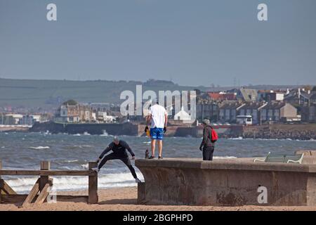 Portobello, Edinburgh, Schottland, Großbritannien. April 2020. Sehr ruhige Promenade und Strand, Temperatur 11 Grad mit Wind ENE 15mph, mögliche Böen von 23 mph, wie die NHS danke Flagge zeigt. Fußgänger mischten sich mit Radfahrern auf der Promenade oft zu eng für richtige körperliche soziale Distanz und wenige Menschen am Sandstrand. Quelle: Arch White/Alamy Live News. Stockfoto