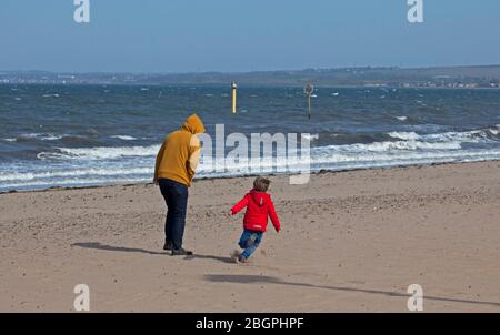 Portobello, Edinburgh, Schottland, Großbritannien. April 2020. Sehr ruhige Promenade und Strand, Temperatur 11 Grad mit Wind ENE 15mph, mögliche Böen von 23 mph, wie die NHS danke Flagge zeigt. Fußgänger mischten sich mit Radfahrern auf der Promenade oft zu eng für richtige körperliche soziale Distanz und wenige Menschen am Sandstrand. Quelle: Arch White/Alamy Live News. Stockfoto