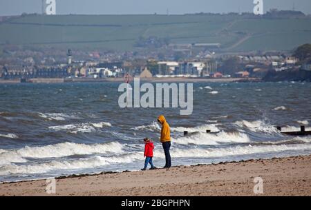 Portobello, Edinburgh, Schottland, Großbritannien. April 2020. Sehr ruhige Promenade und Strand, Temperatur 11 Grad mit Wind ENE 15mph, mögliche Böen von 23 mph, wie die NHS danke Flagge zeigt. Fußgänger mischten sich mit Radfahrern auf der Promenade oft zu eng für richtige körperliche soziale Distanz und wenige Menschen am Sandstrand. Quelle: Arch White/Alamy Live News. Stockfoto