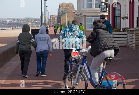 Portobello, Edinburgh, Schottland, Großbritannien. April 2020. Sehr ruhige Promenade und Strand, Temperatur 11 Grad mit Wind ENE 15mph, mögliche Böen von 23 mph, wie die NHS danke Flagge zeigt. Fußgänger mischten sich mit Radfahrern auf der Promenade oft zu eng für richtige körperliche soziale Distanz und wenige Menschen am Sandstrand. Quelle: Arch White/Alamy Live News. Stockfoto