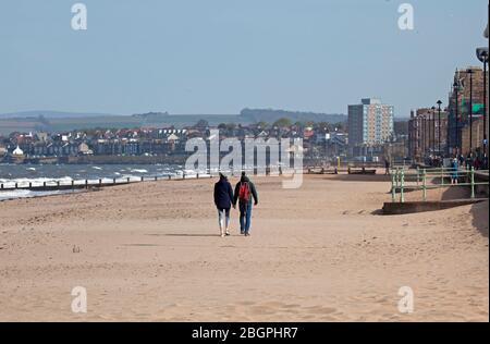 Portobello, Edinburgh, Schottland, Großbritannien. April 2020. Sehr ruhige Promenade und Strand, Temperatur 11 Grad mit Wind ENE 15mph, mögliche Böen von 23 mph, wie die NHS danke Flagge zeigt. Fußgänger mischten sich mit Radfahrern auf der Promenade oft zu eng für richtige körperliche soziale Distanz und wenige Menschen am Sandstrand. Quelle: Arch White/Alamy Live News. Stockfoto