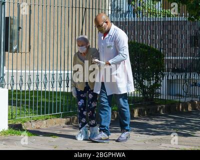 Ältere Frau, die mit Hilfe eines medizinischen Fachs im Freien bei einem Ausbruch des Coronavirus Gesichtsmasken und Handschuhe verwendet. Pflegekraft in Brasilien. Stockfoto