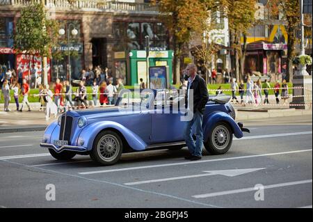 Mann, Fahrer, sitzt im Retro-Auto, Menschenmenge verschwommen auf einem Hintergrund Stockfoto