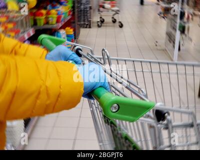 Frauen Hände in medizinischen Schutzhandschuhen Handschuhe halten den Griff des Lebensmittellackwagens, close-up. Coronavirus-Schutz im Supermarkt Stockfoto