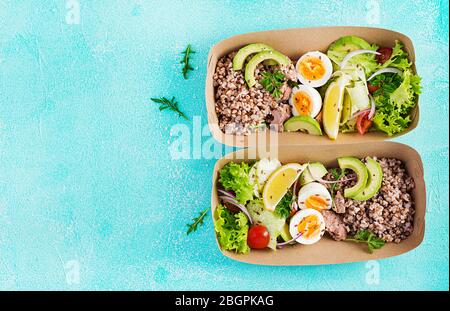 Gesunde Lebensmittel liefern. Mittagessen - Buchweizenbrei, Thunfisch in Scheiben geschnitten, gekochtes Ei und frischen Gemüsesalat in Null Abfallbehälter auf blauem Hintergrund. Oben Stockfoto