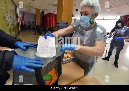 Ein Freiwilliger aus dem Rathaus von El Vendrell, der eine chirurgische Maske und Schutzhandschuhe trägt, liefert eine Person, die nach der Schließung von sozialen Esszimmern aufgrund der Pandemie von Covid-19 Sozialdienst leistet, Lebensmittel an eine Person, die Sozialhilfe erhalten hat. Das Ministerium für Sozialdienste des Stadtrats von El Vendrell (Tarragona Spanien) Verteilt rund 70 Personen an Lebensmitteln, die an Menschen der sozialen Hilfe vergeben werden. Die Santa Teresa Private Foundation und die Freiwilligen der School of Hospitality von Santa María del Mar von El Vendrell bereiten die Catering-Art von Menüs und das Essen aufgrund der Sicherheitsmaßnahmen der Covid-19 Pandemie. Stockfoto