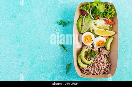 Gesunde Lebensmittel liefern. Mittagessen - Buchweizenbrei, Thunfisch in Scheiben geschnitten, gekochtes Ei und frischen Gemüsesalat in Null Abfallbehälter auf blauem Hintergrund. Oben Stockfoto