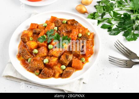 Rinderbraten mit Kartoffeln und Karotten in Tomatensauce auf weißem Teller Stockfoto