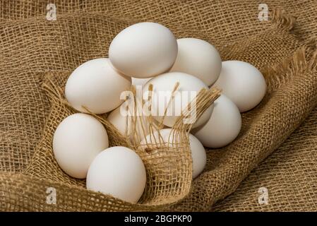 Weiße Hühnereier in Burlap neben einem Korb auf einem weißen Eier auf Burlap Hintergrund gewickelt Stockfoto