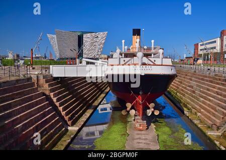 Irland, Grafschaft Antrim, Belfast, Titanic Quarter, Titanic Belfast Besucherattraktion mit der SS Nomadic eine ehemalige Ausschreibung für die Reederei White Star Line, die einst für den Transport von Post und Passagieren zur und von der Titanic im Vordergrund verwendet wurde. Stockfoto