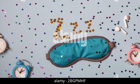 Blaue Schlafaugen-Maske und Wecker auf blauem Hintergrund mit kleinen Sternen. Ruhe, gute Nacht, Siesta, Schlaflosigkeit, Entspannung, müde, Reisekonzept Stockfoto