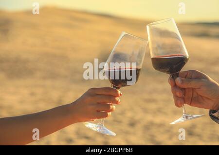 Hände halten Rotweingläser auf Dune von Pyla während des Sonnenuntergangs, Feier Konzept Stockfoto