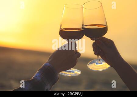 Hände halten Rotweingläser auf Dune von Pyla während des Sonnenuntergangs, Feier Konzept Stockfoto