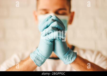 Der katholische Arzt in medizinischer Gesichtsmaske und Schutzhandschuhen betet im Krankenhaus zu Gott. Junger Mann christian Gebet in medizinischen Handschuhen und schützen Stockfoto