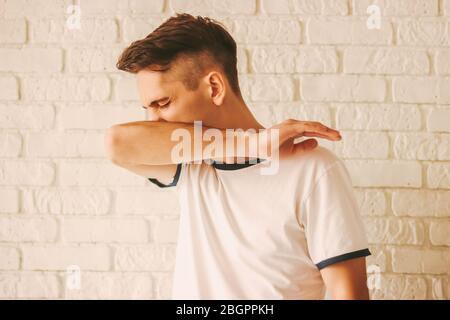 Junger kranker Mann, der Mund und Nase mit Arm bedeckt, während er zu Hause niest. Infizierter Mann Patient hustet im Ellenbogen. Vermeiden Sie die Verbreitung des Coronavirus COVID-19. Stockfoto