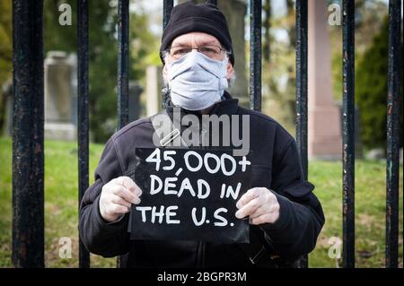 Brooklyn, Vereinigte Staaten Von Amerika . April 2020. Ein Mitglied der gewaltfreien politischen Aktionsgruppe "Rise and Resist" hält ein Schild mit der Anzahl der Menschen, die bisher in den Vereinigten Staaten von Amerika vor dem Greenwood Cemetery in Brooklyn, NY, am 22. April 2020 an dem Coronavirus gestorben sind. (Foto Gabriele Holtermann-Gorden/Sipa USA) Quelle: SIPA USA/Alamy Live News Stockfoto