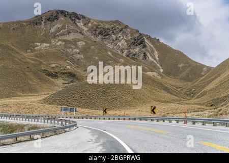 Landschaft mit Straße 8 Biegen unter kargen Hängen in der Berglandschaft, in hellen Frühlingslicht in der Nähe Lindis Pass, Otago, Südinsel, New Eifer aufgenommen Stockfoto