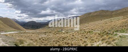 Landschaft mit Straße 8 und Pfad auf kargen Hängen in der Berglandschaft, aufgenommen in hellen Frühlingslicht am Lindis Pass, Canterbury, South Island, Neuseeland Stockfoto