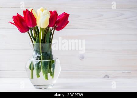 Blumenstrauß von Tulpen in Vase auf weißem Holzbrett Hintergrund. Leere Stelle für Text. Blumenrahmen, Holzhintergrund. Geschenkkarte mit Kopierfläche, Modell Stockfoto