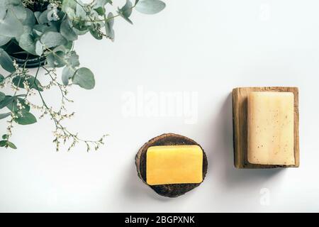 Seifenstücke auf Holzbalken mit Eukalyptus und Kräutern in der Ecke auf weißem Papier Hintergrund mit Kopierraum. Gesundheits- und Schönheitskonzept. Stockfoto