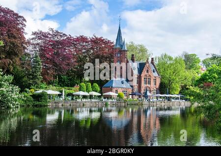 Blick auf die ruhige öffentliche Grünfläche mit Minnewater Lake und kleinem Schloss in Brügges während des sonnigen Frühlingstages in Belgien Stockfoto