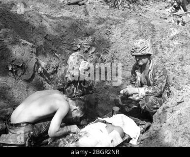 Ein verwundete US-Marineinfanterist, der Blutplasma erhielt, während er auf einer Bahre in einem Graben der erste-Hilfe-Station nahe dem Strand von Bouganville, Empress Augustus Bay, lag, November 1943. Ein Handtuch wurde auf das Gesicht des Patienten gelegt, um die Fliegen abzuhalten. Die amerikanischen Streitkräfte hatten die Insel vor kurzem von den Japanern eingenommen. Dieser Schlitzgraben wurde als minimaler Schutz gegen ständige japanische Flugzeuge straffing Angriffe gegraben. Um meine anderen WW II-bezogenen Bilder zu sehen, Suche: Prestor Vintage WW II Stockfoto