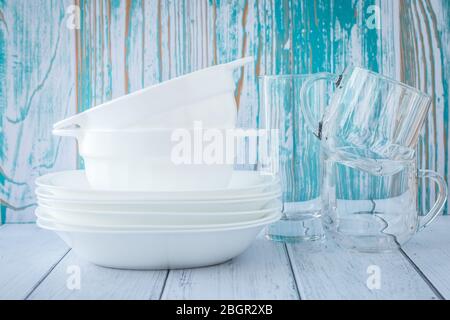 Ein Stapel von sauberen Geschirr auf einem türkisfarbenen Holzhintergrund. Weiße Keramikplatten und transparente Gläser Stockfoto