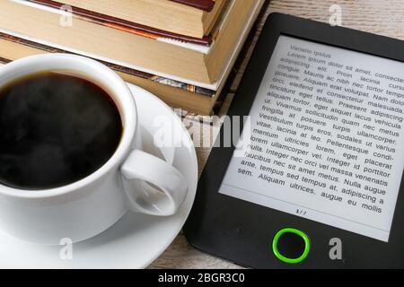 Nahaufnahme des E-Book-Lesers in der Nähe einer Tasse heißen Kaffees und eines Stapels gewöhnlicher Papierbücher. Platz auf E-Book-Anzeige kopieren. E-Reading für Vergnügen und Bildung Stockfoto